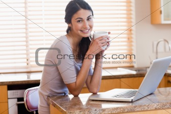 Charming woman using a laptop while drinking a cup of a coffee