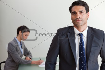 Handsome businessman posing while his colleague is working