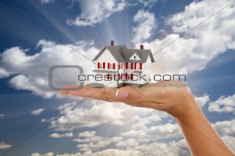 Model House in Female Hand on a Cloud and Sky Background.