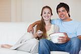 Young couple watching television while eating popcorn