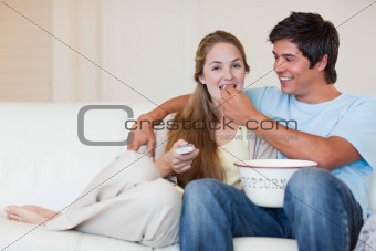 Happy couple watching television while eating popcorn