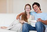 Smiling couple watching television while eating popcorn