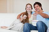 Laughing couple watching television while eating popcorn