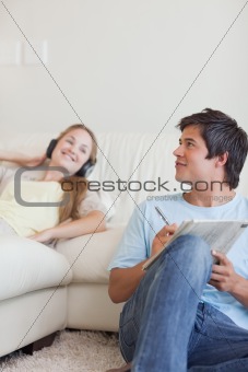Portrait of a man doing crosswords while his girlfriend is listening to music
