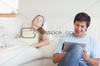 Young man using a tablet computer while his girlfriend is sleeping