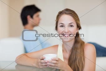 Woman drinking tea while her fiance is sitting on a couch