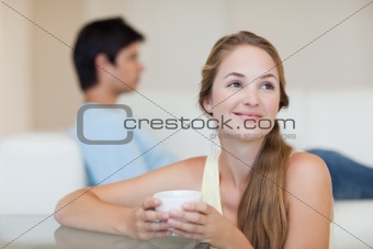 Woman drinking coffee while her fiance is sitting on a couch