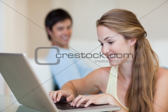 Woman using a notebook while her fiance is sitting on a couch