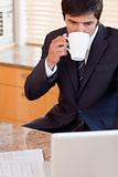 Portrait of a businessman drinking coffee while using a laptop