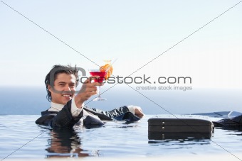 Cheerful businessman relaxing in a swimming pool with a cocktail