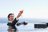 Delighted businessman relaxing in a swimming pool with a cocktail