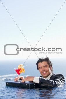 Portrait of a businessman relaxing in a swimming pool with a cocktail