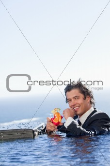 Portrait of a smiling businessman relaxing in a swimming pool with a cocktail