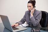 Businesswoman typing on laptop while talking on the phone