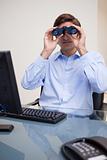 Businessman looking through binoculars in his office