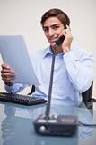 Smiling businessman holding paperwork while on the phone
