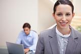 Smiling businesswoman with colleague working on his laptop behind her