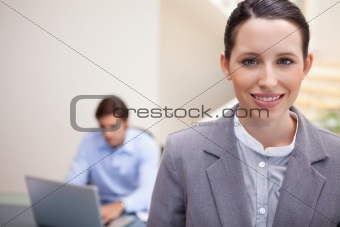 Smiling businesswoman with colleague working on his laptop behind her