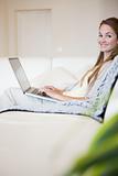 Side view of smiling woman with her laptop sitting on the sofa