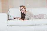 Side view of woman lying on her sofa with her laptop