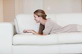 Side view of woman lying on the couch working on her laptop