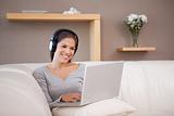 Smiling woman with headphones and laptop on the sofa