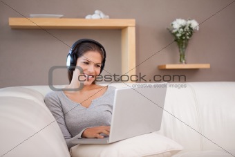 Smiling woman with headphones and laptop on the sofa