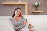 Smiling woman with a red rose sitting on the sofa