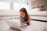 Smiling woman lying with laptop on the floor