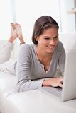 Smiling woman lying on the sofa with her laptop