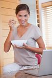 Woman having a bowl of cereals next to her laptop