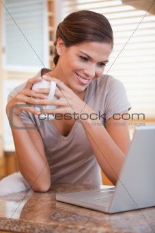 Woman with coffee and laptop in the kitchen