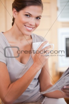 Woman drinking tea while reading newspaper