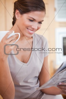 Smiling woman reading newspaper while having tea