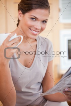 Smiling woman reading the news while drinking coffee