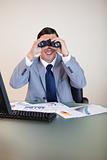 Businessman at his desk looking through binoculars