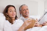 Happy woman reading a book while her husband is reading the news