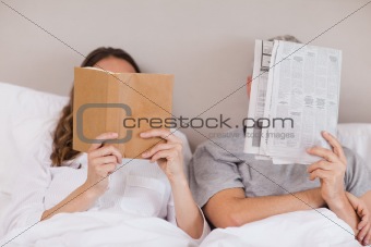 Woman reading a book while her companion is reading a newspaper