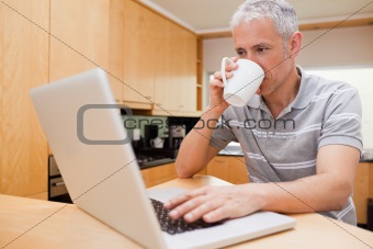 Happy man using a notebook while drinking coffee