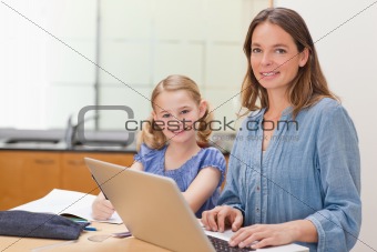 Girl doing her homework while her mother is working with laptop
