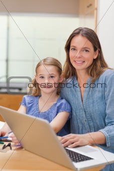 Portrait of a girl doing her homework while her mother is working with laptop