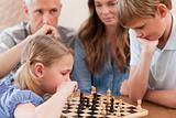 Focused children playing chess in front of their parents