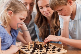 Close up of serious children playing chess in front of their parents