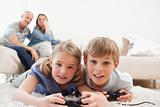 Playful children playing video games with their parents on the background