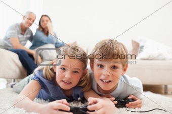 Playful children playing video games with their parents on the background