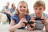 Playful siblings playing video games with their parents on the background