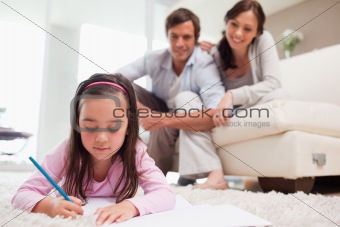 Little girl drawing with her parents in the background