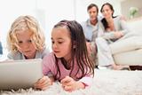 Cute siblings using a tablet computer while their parents are in the background