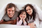 Parents lying under a duvet with their daughter