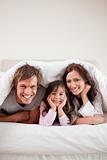 Portrait of parents lying under a duvet with their daughter